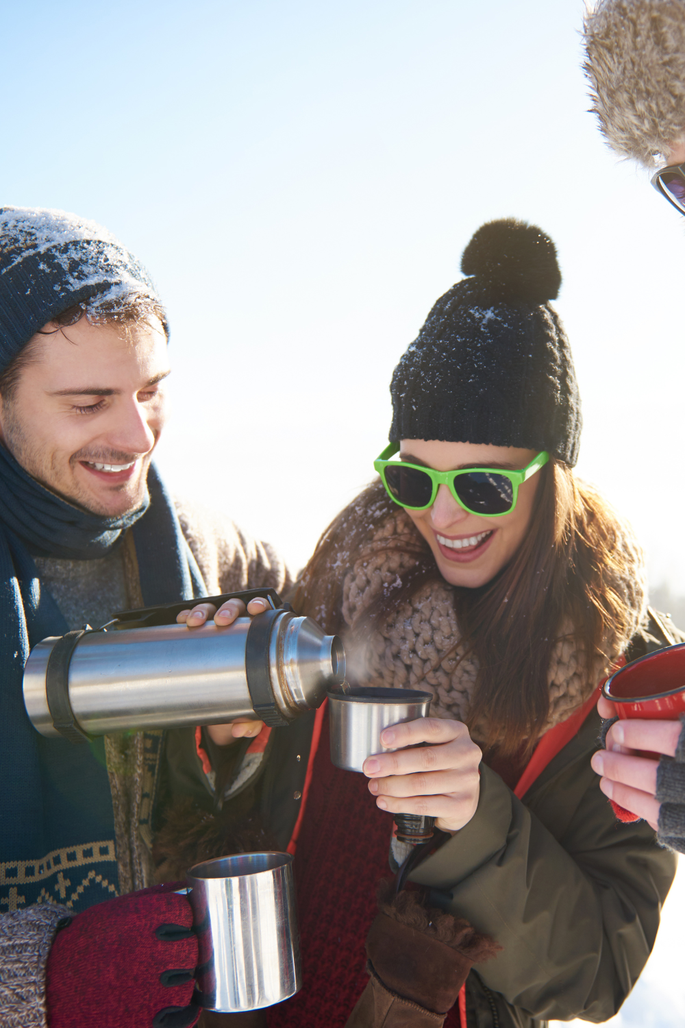 Friends sharing a hot drink from a thermos during a winter ski trip in the French Alps
